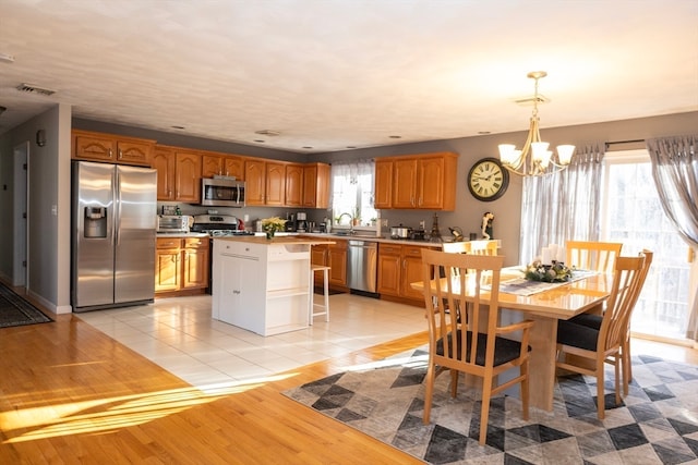 kitchen with a center island, stainless steel appliances, an inviting chandelier, light hardwood / wood-style flooring, and decorative light fixtures