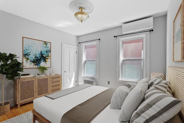 bedroom with an AC wall unit, radiator heating unit, and light wood-style flooring