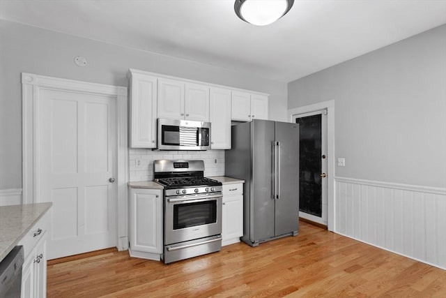 kitchen with light wood finished floors, appliances with stainless steel finishes, white cabinets, and tasteful backsplash