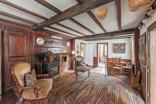 living area with a fireplace, beam ceiling, light hardwood / wood-style floors, and a wood stove