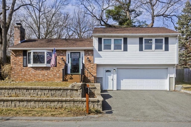 split level home with brick siding, driveway, a chimney, and a garage