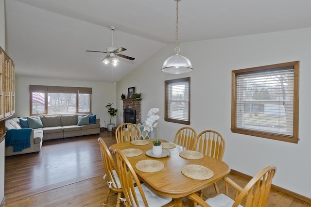 dining space with baseboards, light wood finished floors, lofted ceiling, ceiling fan, and a brick fireplace