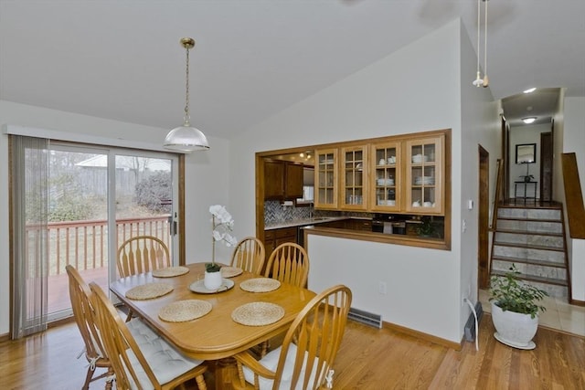 dining area with baseboards, light wood finished floors, stairs, and vaulted ceiling