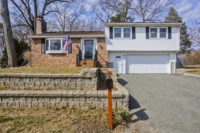 split level home with aphalt driveway, a chimney, a garage, and brick siding