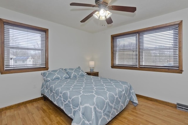 bedroom with multiple windows, wood finished floors, and baseboards