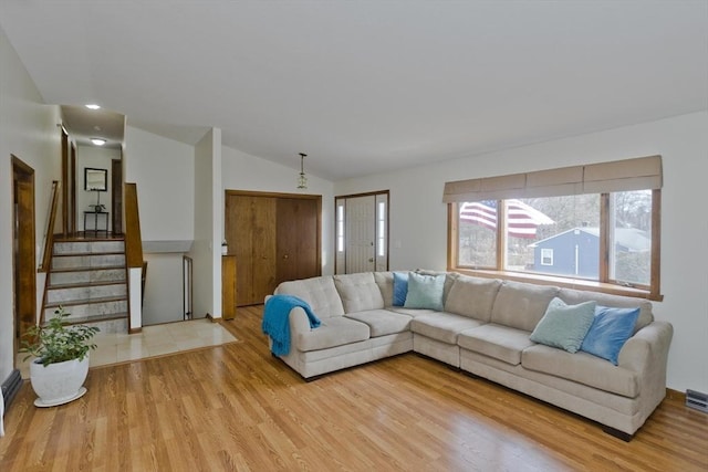 living area with stairway, visible vents, light wood-style floors, and vaulted ceiling