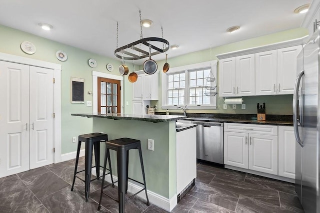 kitchen with appliances with stainless steel finishes, a breakfast bar area, white cabinetry, and dark marble finish floors