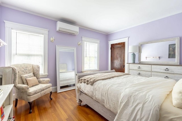 bedroom with a wall unit AC, light wood-style flooring, crown molding, and baseboards