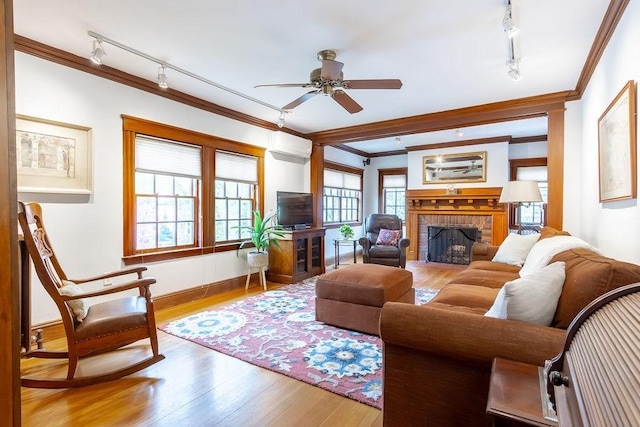 living room featuring rail lighting, ornamental molding, a fireplace, a ceiling fan, and wood finished floors