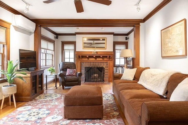 living area featuring rail lighting, a wall unit AC, a ceiling fan, a brick fireplace, and crown molding