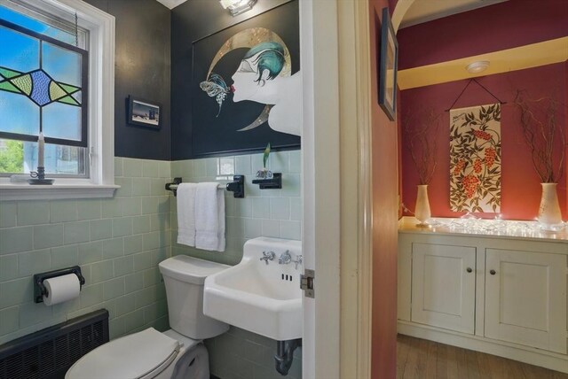 128 Lovell Rd, Holden, MA 01520 - half bathroom with tile walls, radiator heating unit, toilet, a sink, and wood finished floors