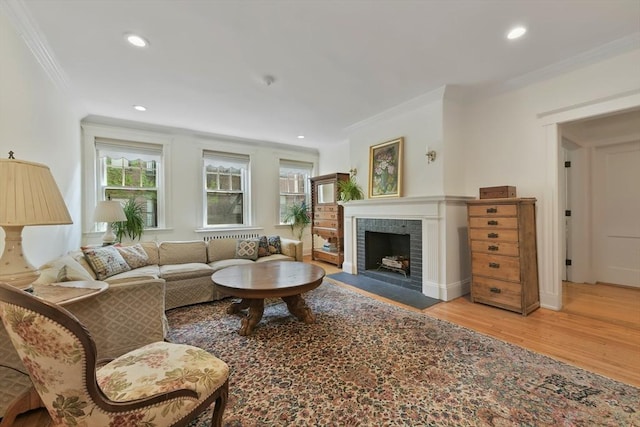 living room with ornamental molding, wood finished floors, healthy amount of natural light, a tiled fireplace, and recessed lighting
