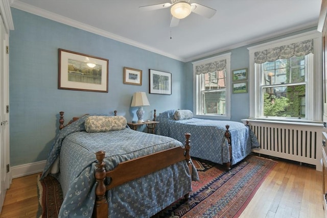 bedroom with radiator, hardwood / wood-style flooring, ornamental molding, baseboards, and a ceiling fan