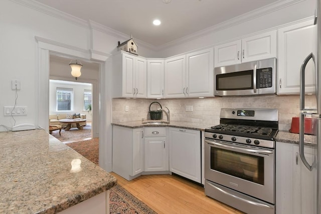 kitchen featuring appliances with stainless steel finishes, white cabinetry, a sink, ornamental molding, and light wood-style flooring