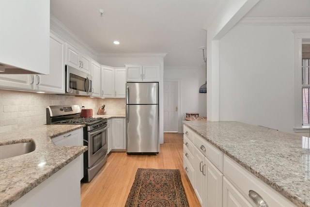 kitchen with stainless steel appliances, light wood-style floors, white cabinets, light stone countertops, and crown molding