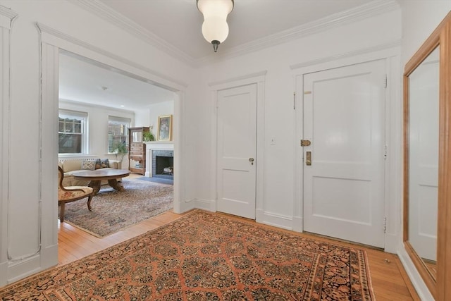 foyer entrance featuring light wood-type flooring, a fireplace with flush hearth, and crown molding