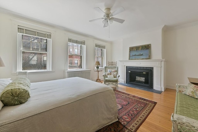 bedroom featuring radiator, wood finished floors, a fireplace with flush hearth, and a ceiling fan