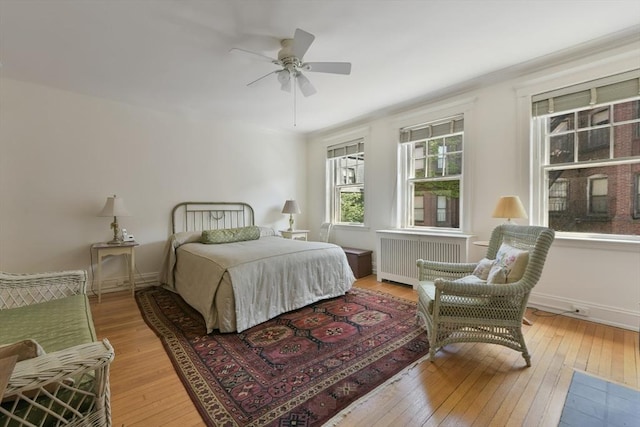 bedroom featuring radiator heating unit, light wood-type flooring, baseboards, and ceiling fan