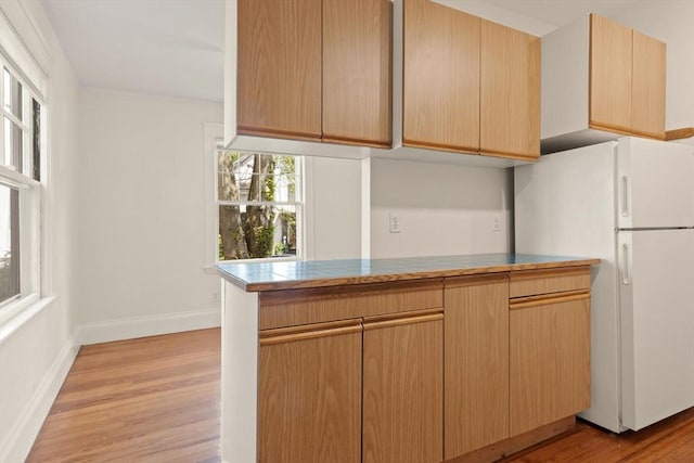 kitchen featuring freestanding refrigerator, light wood finished floors, baseboards, and light brown cabinetry