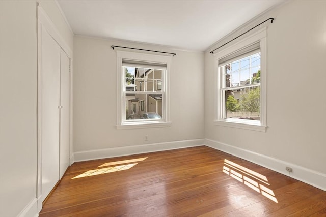 unfurnished bedroom featuring hardwood / wood-style floors, multiple windows, baseboards, a closet, and crown molding