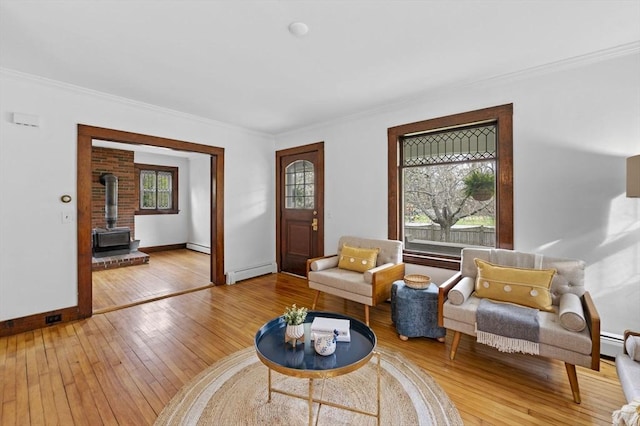sitting room with a baseboard radiator, ornamental molding, a wood stove, and light wood finished floors