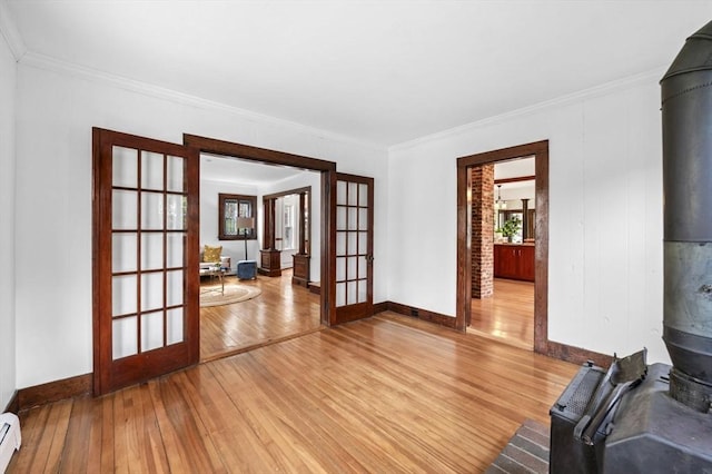 unfurnished living room with crown molding, a wood stove, french doors, light wood-type flooring, and a baseboard radiator