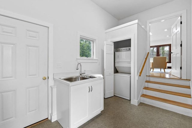 laundry room featuring laundry area, plenty of natural light, a sink, and stacked washer and clothes dryer