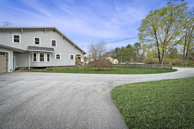 view of side of property with aphalt driveway, fence, and a yard