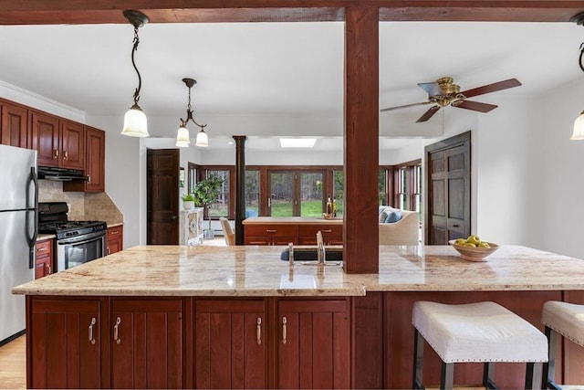 kitchen with decorative backsplash, under cabinet range hood, a ceiling fan, appliances with stainless steel finishes, and hanging light fixtures