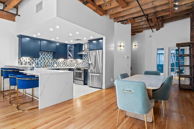 dining area featuring a towering ceiling, beam ceiling, sink, and light hardwood / wood-style flooring