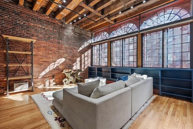 living room with wood ceiling, light hardwood / wood-style flooring, a towering ceiling, brick wall, and beamed ceiling