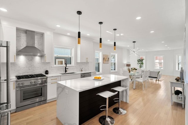 kitchen featuring a kitchen island, appliances with stainless steel finishes, white cabinetry, sink, and wall chimney exhaust hood