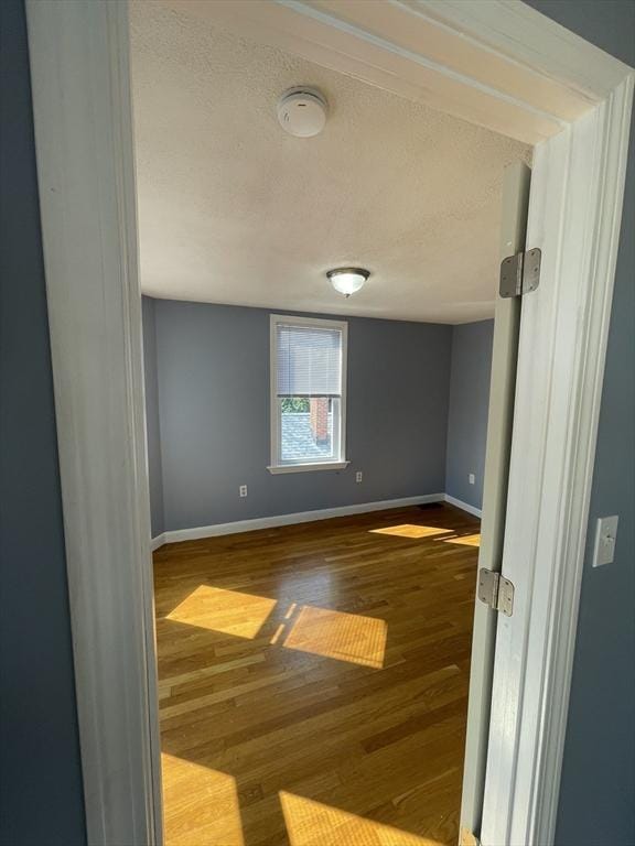 empty room with baseboards, a textured ceiling, and wood finished floors