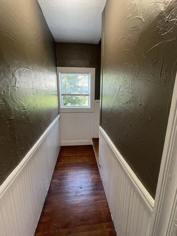 hallway featuring wood finished floors, wainscoting, and a textured wall