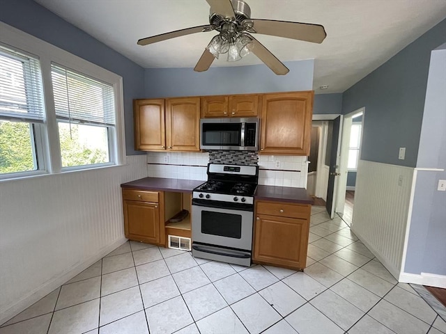 kitchen with dark countertops, visible vents, a wainscoted wall, light tile patterned floors, and appliances with stainless steel finishes