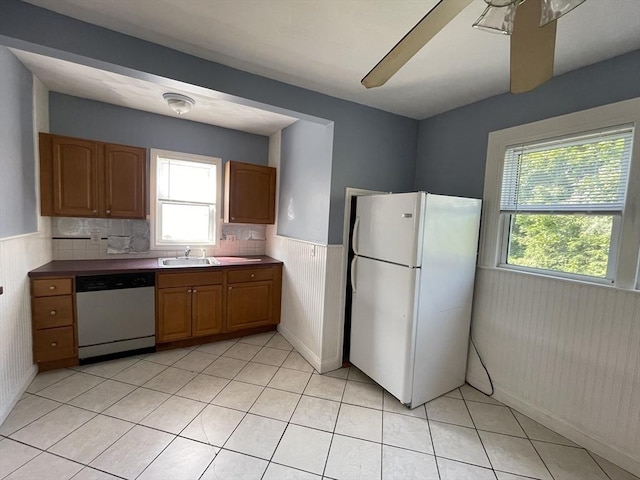 kitchen with a sink, freestanding refrigerator, wainscoting, light tile patterned floors, and dishwasher