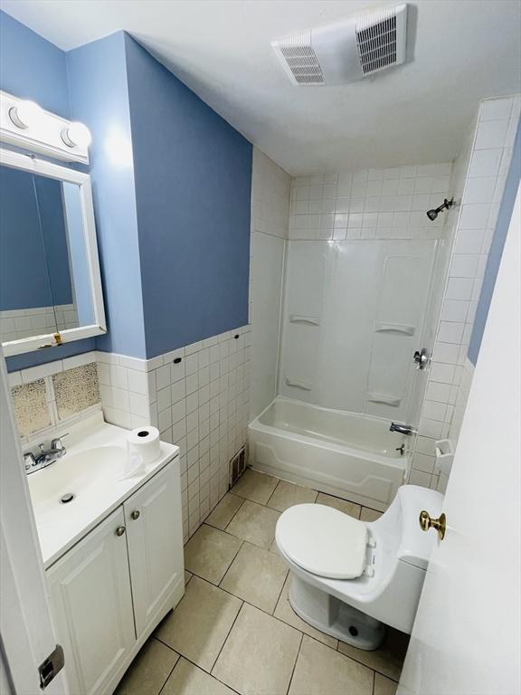 bathroom featuring tile patterned flooring, visible vents, tub / shower combination, wainscoting, and tile walls