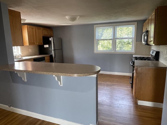 kitchen with decorative backsplash, appliances with stainless steel finishes, a kitchen breakfast bar, and a peninsula