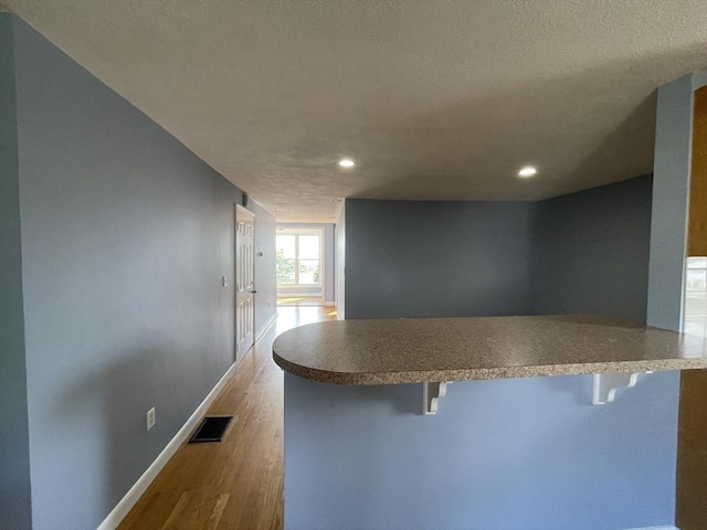 kitchen with visible vents, baseboards, a breakfast bar area, a peninsula, and wood finished floors