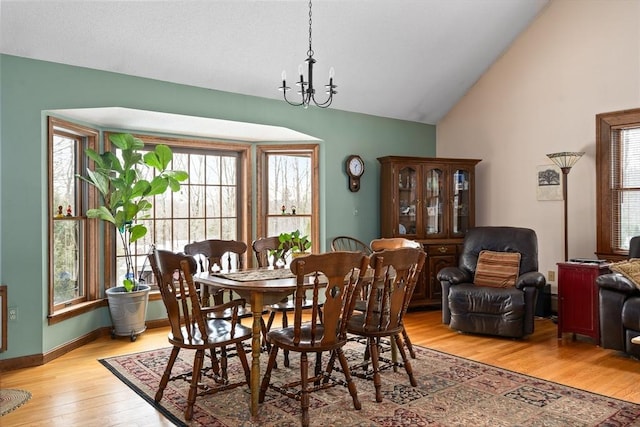 dining space featuring a chandelier, high vaulted ceiling, light wood-type flooring, and baseboards