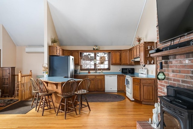 kitchen featuring white appliances, a breakfast bar, a peninsula, under cabinet range hood, and a wall mounted AC