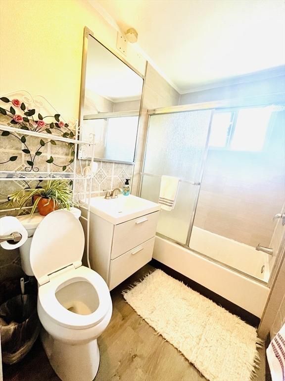 173 Brookway Rd, Boston, MA 02131 - full bathroom featuring vanity, combined bath / shower with glass door, toilet, wood finished floors, and crown molding