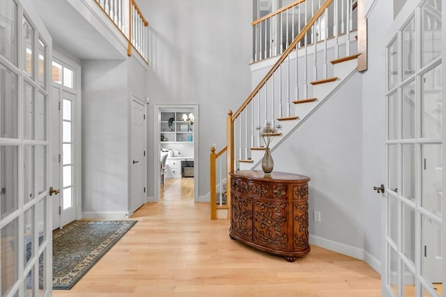 foyer featuring stairway, wood finished floors, baseboards, a high ceiling, and french doors