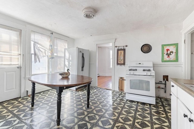 kitchen with white appliances, a textured ceiling, and white cabinets