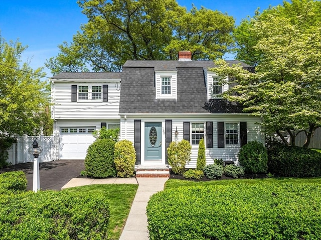 colonial inspired home featuring driveway, an attached garage, roof with shingles, and a chimney