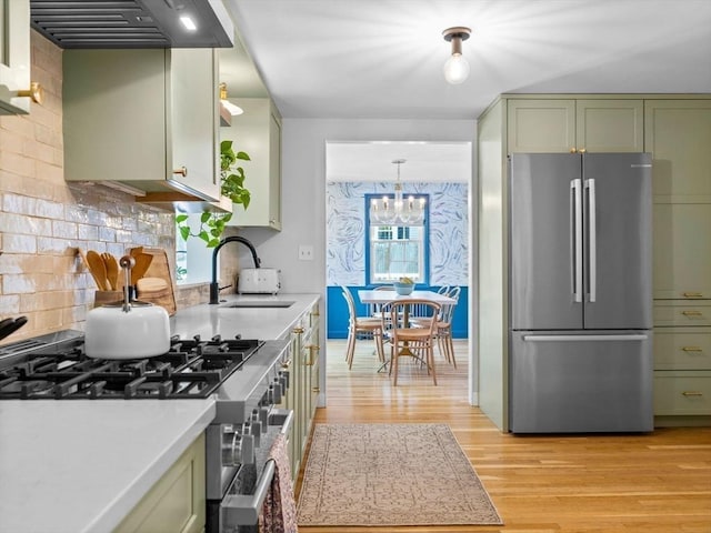 kitchen with appliances with stainless steel finishes, green cabinetry, a sink, premium range hood, and light wood finished floors
