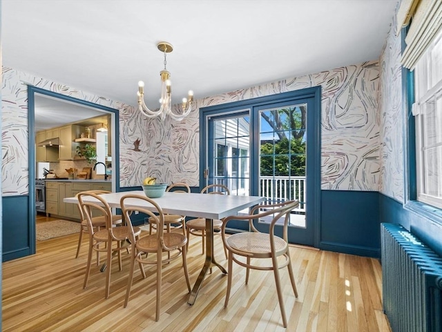 dining area featuring wallpapered walls, radiator heating unit, light wood-style floors, a chandelier, and a wainscoted wall