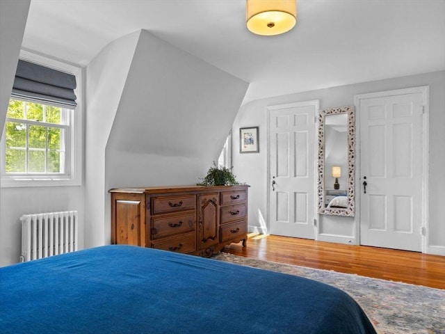 bedroom with radiator, wood finished floors, and baseboards