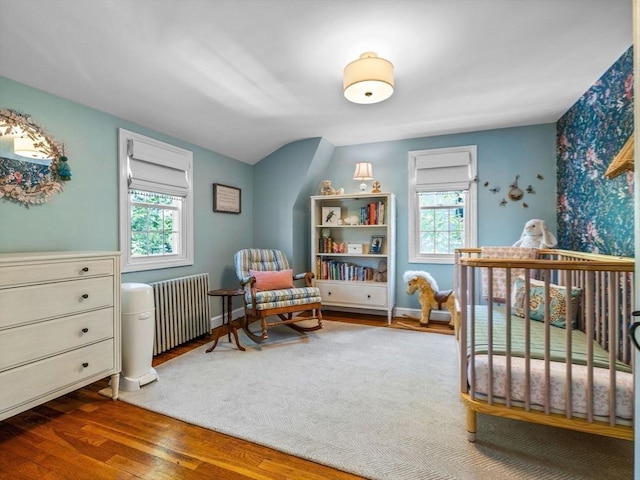 bedroom featuring radiator heating unit, multiple windows, wood finished floors, and a nursery area