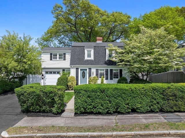 dutch colonial featuring fence, a shingled roof, a chimney, and an attached garage